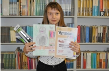Dziewczynka w długich włosach prezentująca dyplom oraz prace plastyczną 
