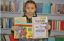 Dziewczynka dumnie prezentująca dyplom oraz prace plastyczną 