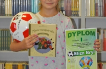 Eliza Bryl trzymająca nagrodyy za udział w konkursie, na tle regsału z ksiażkami