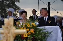 Starostowie dożynkowi siedza za stołem na scenie, na stoliku stoi chleb. W tle zespół ludowy 