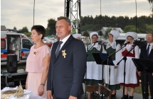 Starostowie dożynkowi stojąna scenie, w tle zespół ludowy Tradycja