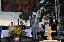 Przemawaijacy wójt na scenie, obok konferansjerzy oraz starostowie dożynek siedzący za stołem