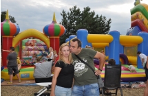 Mezczyzna daje buziaka kobiecie. patrzą w obiektyw, za nimi w tle dzieci bawią się na dmuchańcach