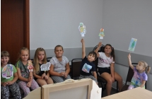 Dzieci siedza na krzeslach, w rekach trzymaja papierowe pstacie z bajek