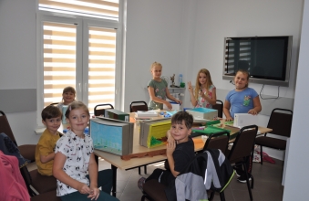 Siedmioro dzieci przy stole w trakcie zajęć plastycznych, patrzą w obiektyw