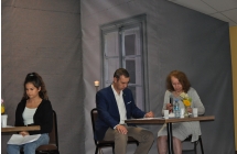 Mezczyzna oraz kobieta siedza przy stole, obok przy drugim stoliku siedzi dziewczyna