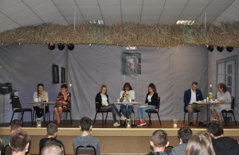 Siedmioro lektorów siedzi na scenie przy stolikach
