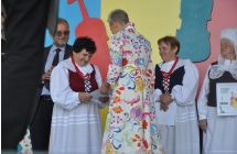Anna Kłodawska z zespołu Jarzębinki na scenie odbiera nagrodę z rąk dyrektor Centrum Kultury i Sztuki w Koninie. W tle inni nagrodzeni uczestnicy festiwalu i jurorzy.
