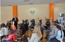 Zbigniew Kolba zadaje pytanai uczestnikom spotkania, wsrod siedzacych uczniow kilkoro trzyma rece w gorze zlgaszajac sie do odpowiedzi
