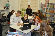 Uczestnicy Nocy Detektywow roziwazuja zagadki we wnetrzu biblioteki, na stoliku stoi laptop wokol ktorego skupiona jest grupka mlodziezy