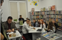 Wnetrze biblioteki. Krzystof Petek przygotowuje zagadki, obok w skupieniu oczekuja uczestnicy Nocy Detektywow.  