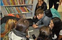 Mlodzi detektywi klecza na wykladzinie w bibliotece, rozwiazuja zagadki zapisane na paskach papieru 