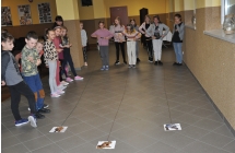 Grupa dzieci z których troje zwija nitki z doczepionymi na końcu papierowymi dinozaurami
