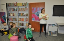 Dzieci siedza na dywanie, obok stoi bibliotekarka