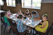 Siedem dziewczynek siedzi przy stole i robi prace plastyczna