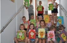 Trzynascioro dzieci siedzi i stoi na schodach trzymajac swoje prace plastyczne