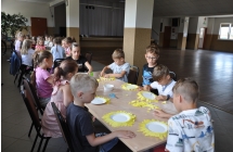 Dzieci siedza przy stolach i wykonuja papierowe sloneczniki