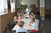 Dzieci przy stole siedza sluchajac pani prowadzacej zajecia (1)