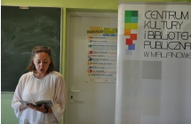 Kobieta czyta trzymana w rekach ksiazke, obok stoi baner CKiBP w Malanowie