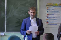 Mezczyzna trzyma w rekach kartke, stoi przed tablica szkolna