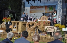 Mezczyzni na scenie oraz wience dozynkowe zlozone pod scena