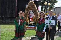Dwie kobiety w ludowych strojach w towarzystwie mezczyzny trzymajacego tabliczke
