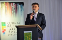 Mężczyzna mówiący do mikrofonu na tle baneru promocyjnego 