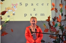 Dziewczynka w pomaranczowej bluzie na scenie, w tle napis spacer z psem