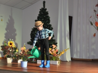 Chłopiec na scenie w słomkowym kapeluszu podlewa kwiatek zieloną konewką