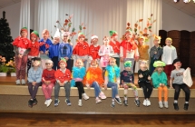 Dwadzieścioro troje dzieci stoi i siedzi na scenie w dwóch rzędach. Są przebrani w kolorowe bajkowe stroje