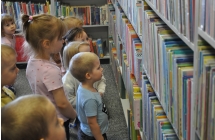 Grupka dzieci stoi wpatrzona w regały z książkami
