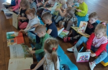 Dzieci siedzą na podłodze w grupie, przeglądają kolorowe książki