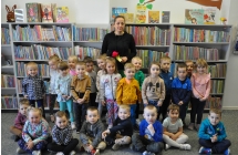 Kobieta wraz z grupą dzieci pozyje na tle regałów z książkami