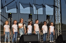 Zespół wokalny na scenie. Kilka młodych dziewczynek w jednakowych strojach 