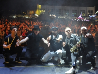 Pięcioro mężczyzn z zespołu muzycznego na tle licznie zgromadzonej publiczności 