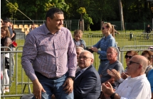 Mężczyzna witający się z ludźmi. Tuż przy nim na ławce zaproszeni goście 