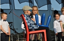 Chłopczyk w kaszkiecie i dziewczynki obok niego. Odgrywają scenkę. 