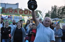 Mężczyzna podnoszący ciężar podczas rywalizacji sportowej. W tle licznie zgromadzona publiczność 
