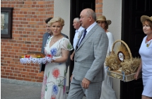 Mężczyzna i kobieta pod kościołem. Kobieta trzyma w dłoniach dożynkowy chleb