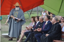 Goście w garniturach oraz mężczyzna w charakterystycznym stroju i zaroście 