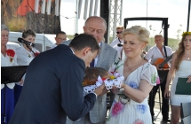 Mężczyzna całujący chleb trzymany przez kobiete, obok nich inny mężczyzna 