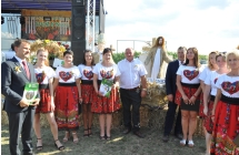Kilkanaście kobiet i mężczyzna przy wieńcu dożynkowym 