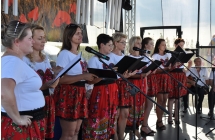 Kilkanaście kobiet w ludowych strojach na scenie śpiewających piosenki 