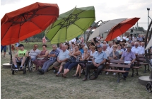 Goście dożynkowi siedzący na ławkach pod sceną.
