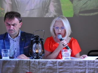 Mężczyzna i kobieta siedzący przy stole. Kobieta mówi do mikrofonu 