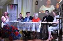 Cztery kobiety i dwoje mężczyzn na scenie. Jedna kobieta i mężczyzna trzymają mikrofony blisko ust 