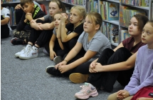Sześć dziewczynek i chłopiec siedzący na podłodze w bibliotece 