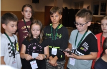 Troje chłopców i dziewczynek. Dzieci mają identyfikatory na szyjach, jeden z chłopców pracuje na tablecie 