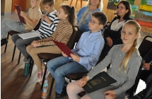 Kilkoro dzieci siedzących na krzesełkach - na sali widowiskowej 