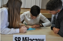 Dziewczynka i dwoje chłopców przy stoliku. Jeden z chłopców pisze na kartce 